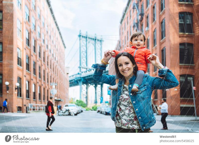 USA, New York, New York City, Mutter und Baby in Brooklyn mit der Manhattan Bridge im Hintergrund auf den Schultern auf der Schulter Tochter Töchter Kindheit
