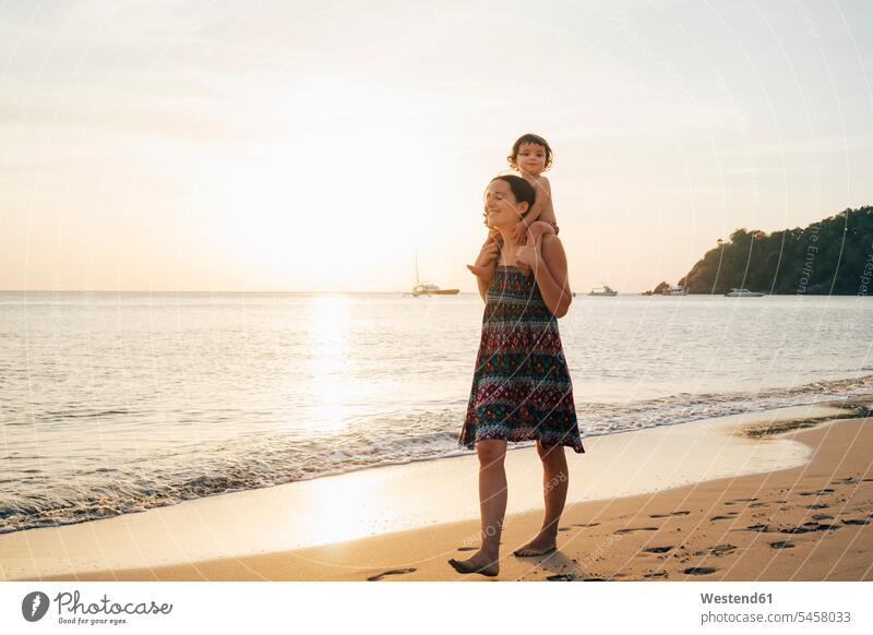 Thailand, Krabi, Koh Lanta, Mutter mit kleiner Tochter auf den Schultern am Strand bei Sonnenuntergang Mami Mutti Mütter Mama Vertrauen vertrauen