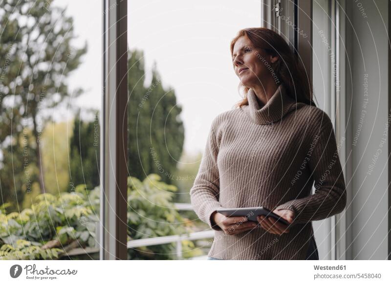 Frau schaut aus dem Fenster und hält ein digitales Tablet Leute Menschen People Person Personen Europäisch Kaukasier kaukasisch 1 Ein ein Mensch eine
