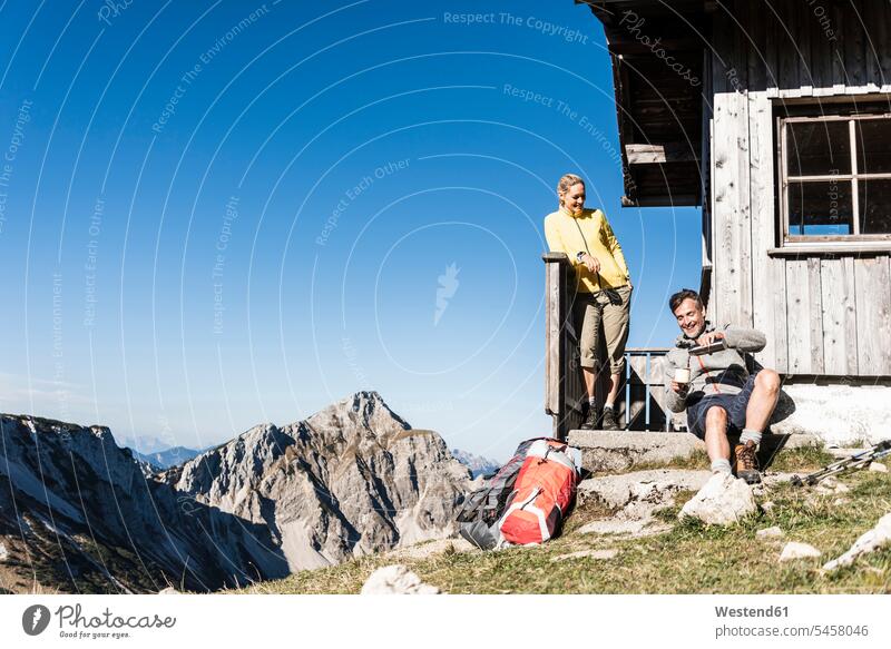 Wanderpärchen vor Berghütte sitzend, eine Pause einlegend Alm Alp Bergweide Almen Bergweiden Alpe Berghütten Berghuette Hütte Gebirge Berglandschaft