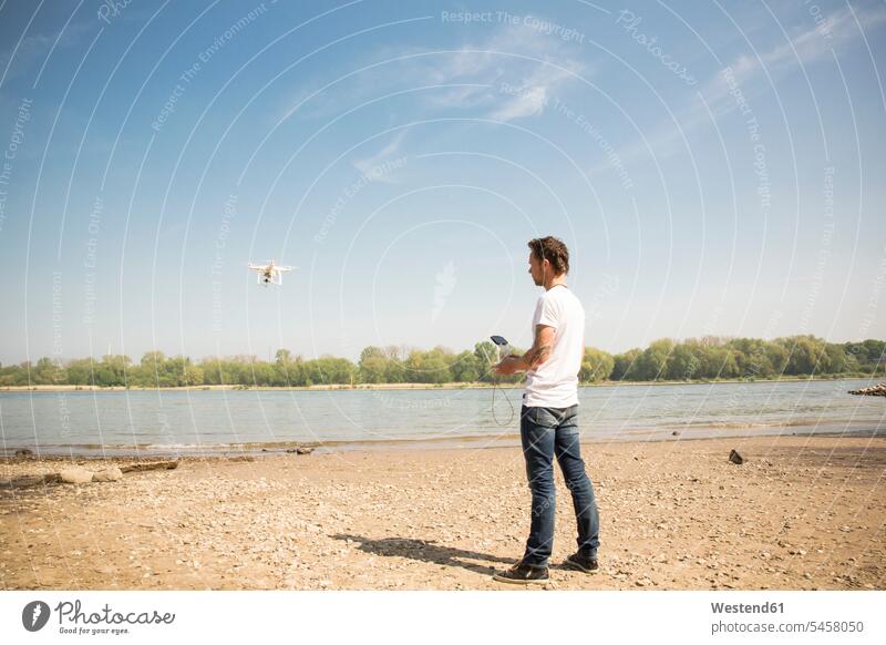 Mann fliegt Drohne an einem Fluss Fluesse Fluß Flüsse Drohnen Männer männlich fliegen fliegend Gewässer Wasser Erwachsener erwachsen Mensch Menschen Leute