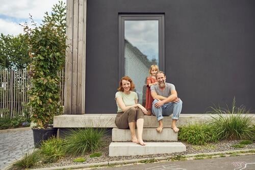 Lächelnde Eltern mit Mädchen auf Stufen vor winzigem Haus sitzend Farbaufnahme Farbe Farbfoto Farbphoto Deutschland Freizeitbeschäftigung Muße Zeit Zeit haben