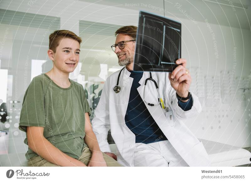 Arzt erklärt Röntgenbild einer gebrochenen Hand für einen Teenager in der medizinischen Praxis Gesundheit Gesundheitswesen Erkrankung Erkrankungen Krankheiten