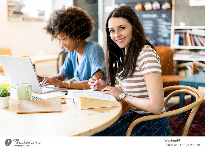 Glückliche Freundinnen lernen mit Laptop am Tisch im Café Farbaufnahme Farbe Farbfoto Farbphoto Innenaufnahme Innenaufnahmen drinnen Tag Tageslichtaufnahme