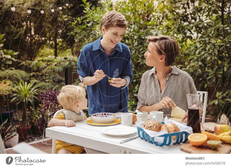 Zwei glückliche Mütter am Frühstückstisch im Freien mit ihrem Kind Glück glücklich sein glücklichsein frühstücken Kinder Frühstückstische Fruehstueckstische