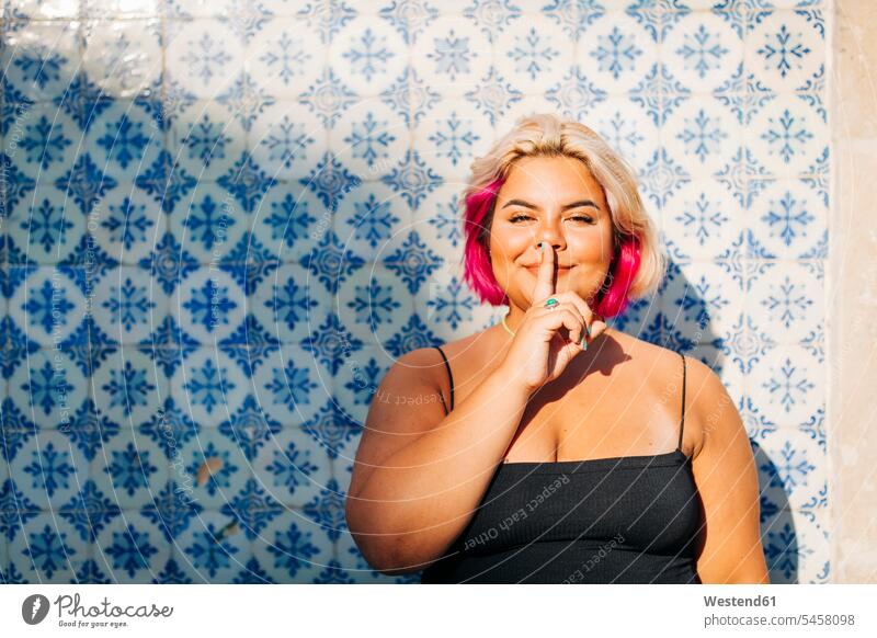 Frau zeigt Schweigezeichen mit dem Finger auf den Lippen an der Wand Farbaufnahme Farbe Farbfoto Farbphoto Außenaufnahme außen draußen im Freien Tag