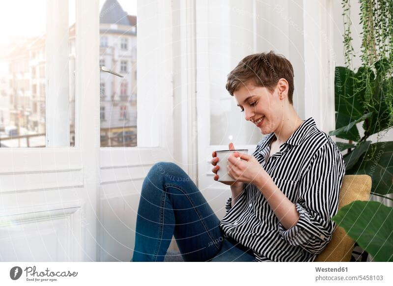 Glückliche Frau sitzt entspannt am Fenster und trinkt Kaffee entspanntheit relaxt glücklich glücklich sein glücklichsein sitzen sitzend trinken weiblich Frauen