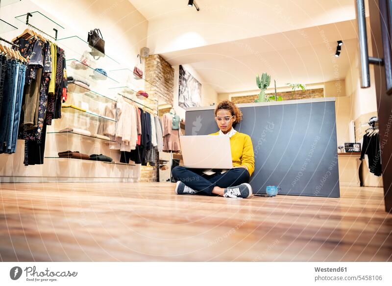 Junge Frau, die in einem Modegeschäft arbeitet und einen Laptop benutzt Verkäuferin Verkaeuferinnen Verkäuferinnen junge Frau junge Frauen Boutique Modeladen