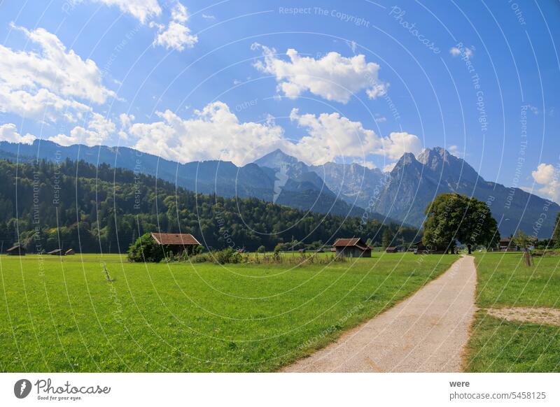 Feldweg bei Garmisch-Partenkirchen mit Blick auf das Zugspitzmassiv an einem sonnigen Tag mit blauem Himmel und weißen Kumuluswolken Deutschland Ansicht Alp