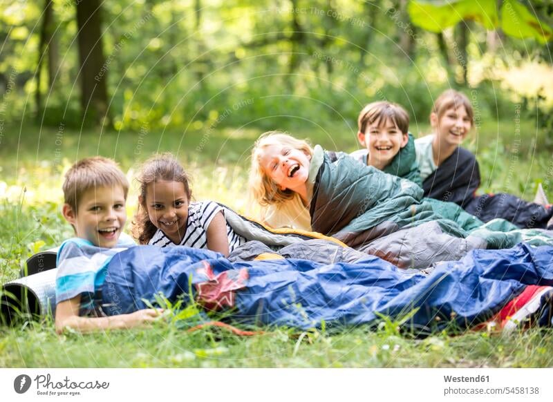 Schulkinder zelten im Wald, liegen in Schlafsäcken lernen Freude grün Camping erkunden Spaß Abenteuer Ausflug Außenaufnahme Tag Blickkontakt lachen positiv