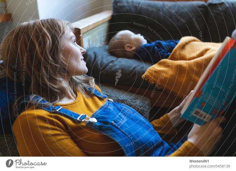 Frau liest Buch im Wohnzimmer, während der kleine Sohn schläft Bücher Couch Couches Liege Sofas Stuehle Stühle entspannen relaxen Lektüre schlafend
