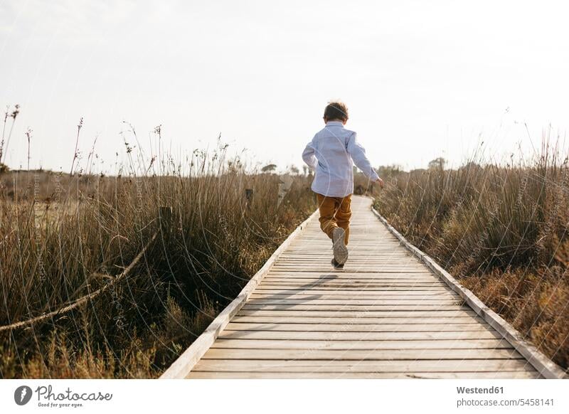 Rückenansicht eines kleinen Jungen, der auf der Promenade läuft Europäer Kaukasier Europäisch kaukasisch Bewegung sich bewegen laufen rennen Holzsteg Holzweg