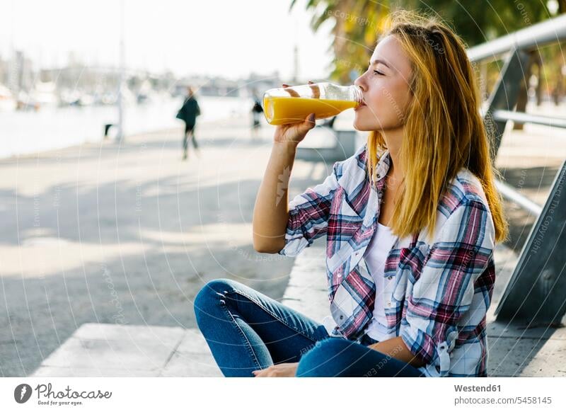 Junge Frau trinkt Saft, während sie auf einem Fußweg in der Stadt sitzt Farbaufnahme Farbe Farbfoto Farbphoto Außenaufnahme außen draußen im Freien Tag