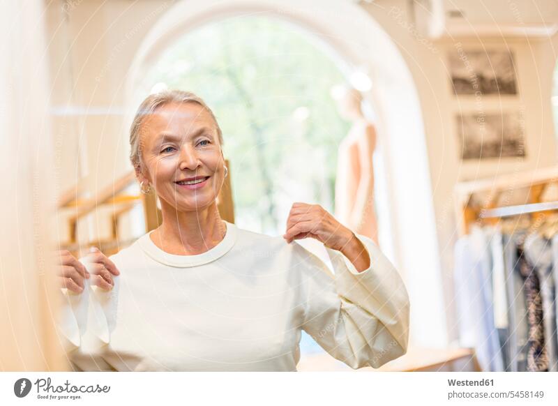Lächelnde Seniorin beim Anprobieren eines Pullovers in einer Boutique älter Seniorinnen alt Shopping einkaufen shoppen Einkauf Frau weiblich Frauen Boutiquen