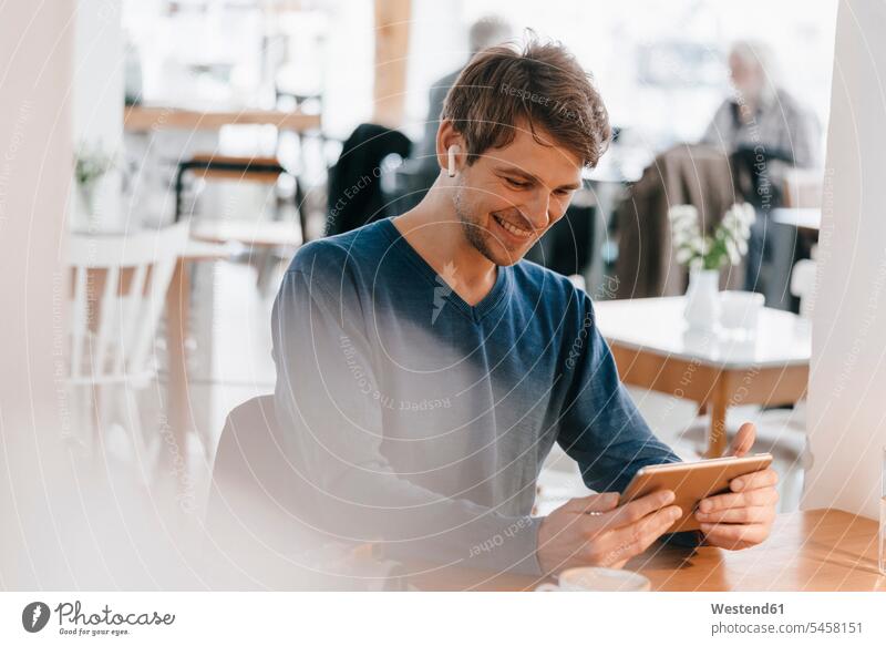 Lächelnder Mann in einem Cafe mit Kopfhörer und Tablette Ohrhörer lächeln Kaffeehaus Bistro Cafes Café Cafés Kaffeehäuser Tablet Computer Tablet-PC Tablet PC