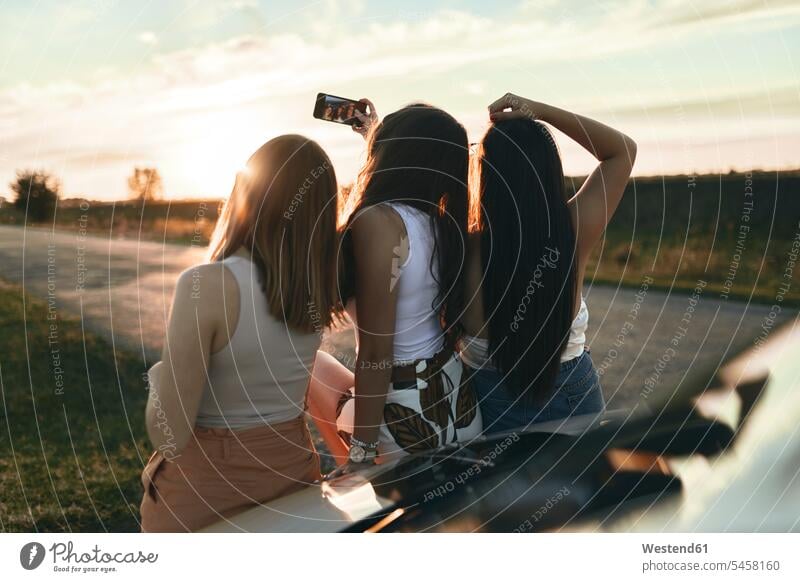 Freundinnen, die bei Sonnenuntergang auf der Straße stehen Farbaufnahme Farbe Farbfoto Farbphoto Außenaufnahme außen draußen im Freien Sonnenuntergänge Stimmung