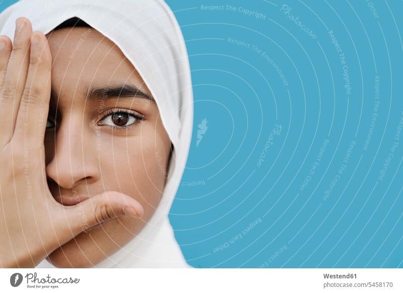 Muslimisches Mädchen bedeckt Auge mit Hand vor blauem Hintergrund Farbaufnahme Farbe Farbfoto Farbphoto Studioaufnahme Studioaufnahmen Innenaufnahme