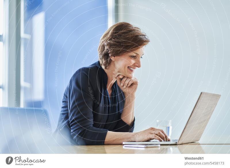 Lächelnde Geschäftsfrau mit Laptop am Schreibtisch im Büro Job Berufe Berufstätigkeit Beschäftigung Jobs geschäftlich Geschäftsleben Geschäftswelt