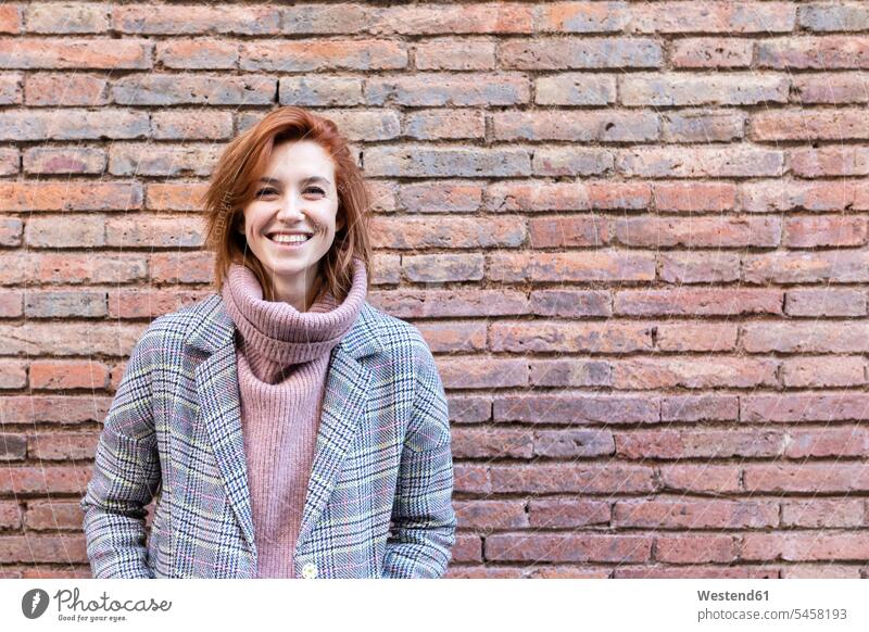 Porträt einer glücklichen jungen Frau, die an einer Backsteinmauer steht weiblich Frauen Wand Wände Waende Backsteinwand Backsteinmauern Portrait Porträts