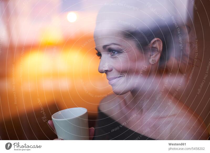 Porträt einer brünetten Frau mit Tasse hinter der Fensterscheibe mit Blick weg Fensterscheiben abends entspannen relaxen entspanntheit relaxt geniessen Genuss