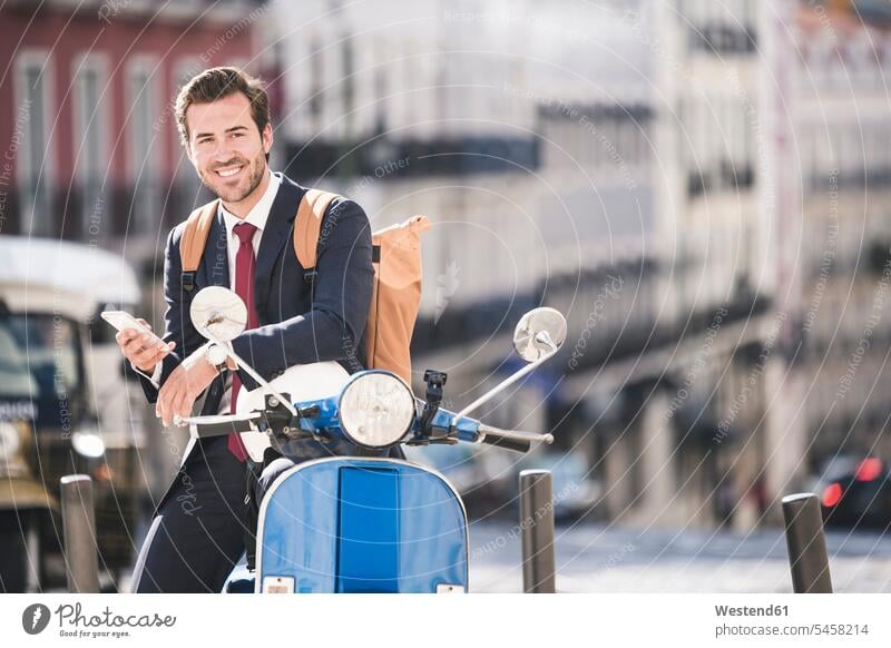Lächelnder junger Geschäftsmann mit Handy und Motorroller in der Stadt, Lissabon, Portugal geschäftlich Geschäftsleben Geschäftswelt Geschäftsperson