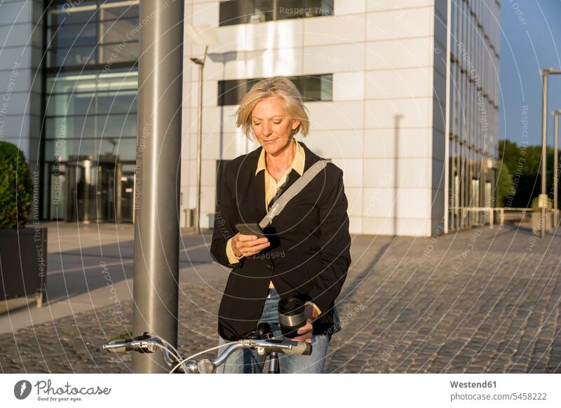 Ältere Frau mit Stadtfahrrad und Kaffee zum Mitnehmen per Handy weiblich Frauen Fahrrad Bikes Fahrräder Räder Rad Mobiltelefon Handies Handys Mobiltelefone