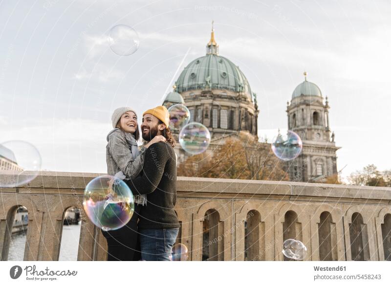Glückliches junges Paar umarmt beim Betrachten von Seifenblasen in der Stadt, Berlin, Deutschland Leute Menschen People Person Personen Europäisch Kaukasier
