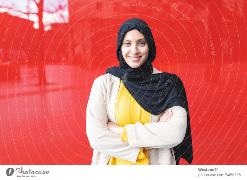 Porträt einer lächelnden jungen Frau, die einen Hijab vor einer roten Glasscheibe trägt Leute Menschen People Person Personen Personen aus dem Nahen Osten 1 Ein