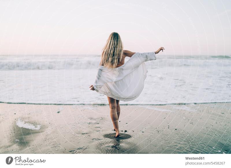 Junge blonde Frau in Bikini und weißem Kleid morgens am Strand Badebekleidung Bikinis Kleider gehend geht früh Frühe Morgen freuen geniessen Genuss Glück