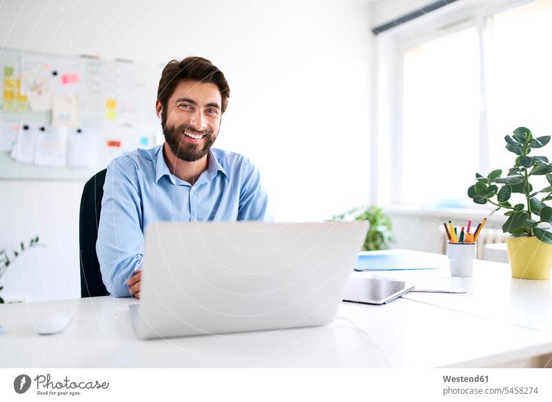 Porträt eines lächelnden Geschäftsmannes, der mit einem Laptop am Schreibtisch sitzt Job Berufe Berufstätigkeit Beschäftigung Jobs Designer geschäftlich