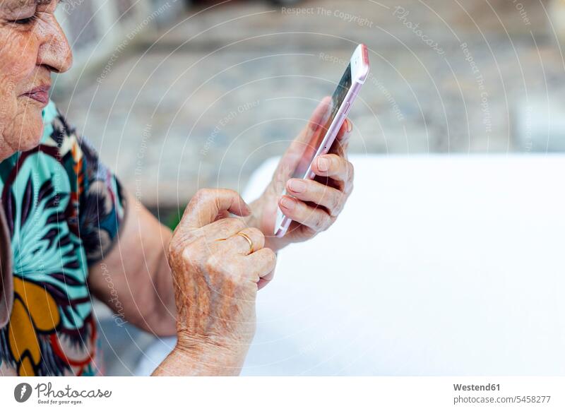 Nahaufnahme einer älteren Frau mit einem Smartphone am Tisch im Hof Farbaufnahme Farbe Farbfoto Farbphoto Spanien Freizeitbeschäftigung Muße Zeit Zeit haben