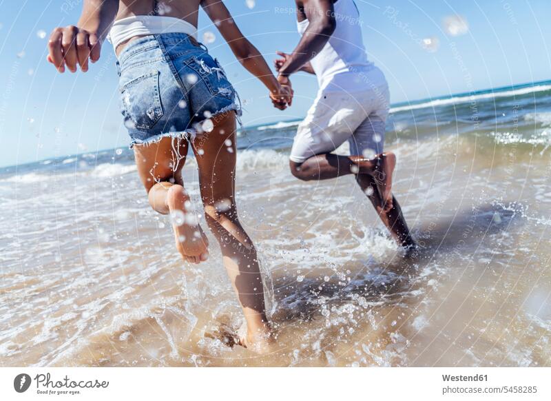 Spielerisches Paar, das sich an den Händen hält, während es im Meer gegen den klaren Himmel rennt Farbaufnahme Farbe Farbfoto Farbphoto Spanien