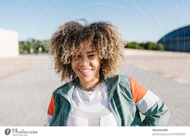 Zuversichtliche junge Frau mit lockigem Haar an einem sonnigen Tag Farbaufnahme Farbe Farbfoto Farbphoto Außenaufnahme außen draußen im Freien