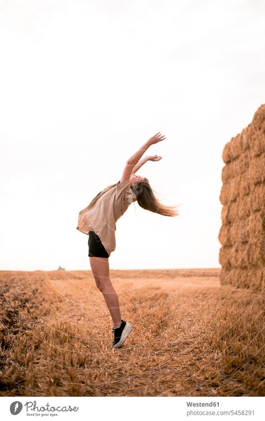 Glückliche junge Frau springt im Feld weiblich Frauen jubeln Jubel schön Felder Heu Heuballen ländlich auf dem Land auf dem Lande Erwachsener erwachsen Mensch