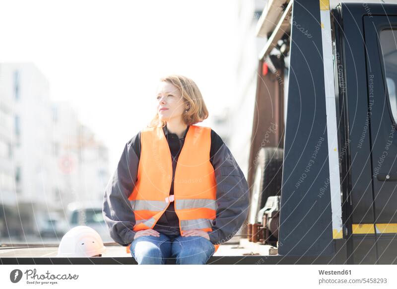 Frau mit reflektierender Weste sitzt auf LKW-Plattform Arbeitshelm Schutzhelm Arbeitshelme Schutzhelme weiblich Frauen Leuchtweste Warnwesten