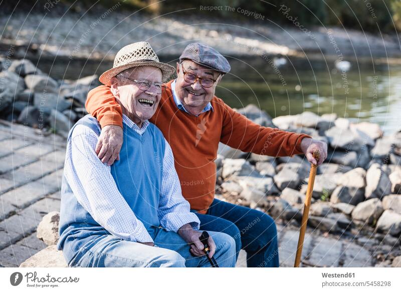 Zwei alte Freunde sitzen am Flussufer und haben Spaß sitzend sitzt Beste Freunde Bester Freund fröhlich Fröhlichkeit Frohsinn Heiterkeit lachen Ufer