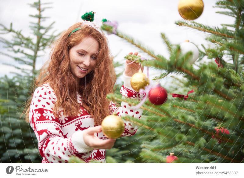 Porträt einer rothaarigen jungen Frau, die im Freien den Weihnachtsbaum schmückt Portrait Porträts Portraits dekorieren weiblich Frauen Christbaum