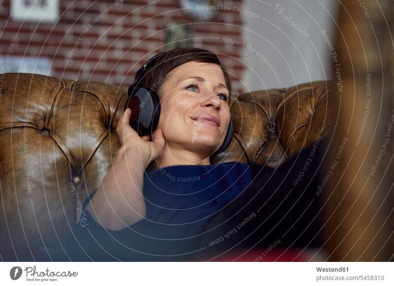 Frau mit Kopfhörer auf dem Sofa liegend, Musik hörend liegt zuhören zuhörend Couches Liege Sofas Kopfhoerer weiblich Frauen hoeren Erwachsener erwachsen Mensch