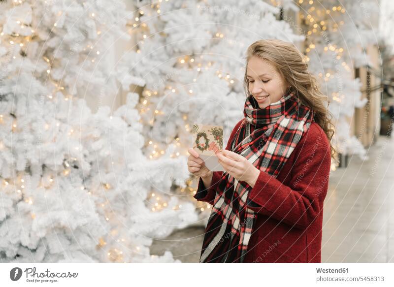 Porträt einer lächelnden jungen Frau, die mit einer Weihnachtskarte vor weißen Weihnachtsbäumen auf der Straße steht Schals Jahreszeiten winterlich Winterzeit