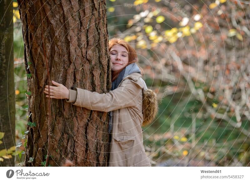 Porträt von lächelnden Teenager-Mädchen umarmt Baumstamm in herbstlichen Wald Portrait Porträts Portraits Forst Wälder Herbstwald Teenagerin junges Mädchen