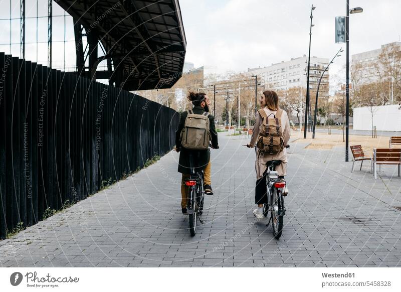 Rückansicht eines Paares, das mit E-Bikes in der Stadt fährt und miteinander spricht radfahren fahrradfahren radeln Fahrrad Fahrräder Räder Rad sprechen reden