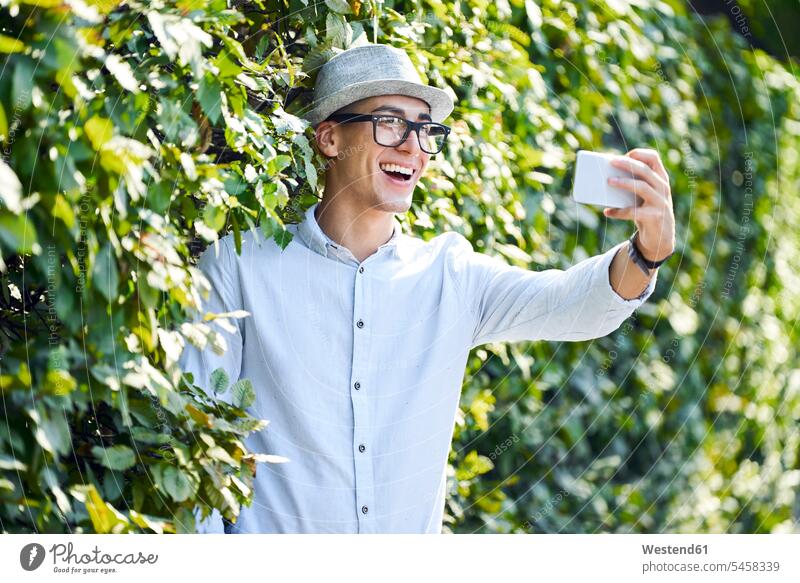 Glücklicher junger Mann macht Selfie in einer Hecke gemischtrassige Person verspielt spielerisch Drahtlose Technologie drahtlose Verbindung