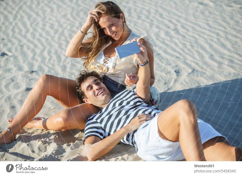 Glückliches, zärtliches, junges Paar macht ein Selfie am Strand Zuneigung Selfies glücklich glücklich sein glücklichsein lächeln Pärchen Paare Partnerschaft