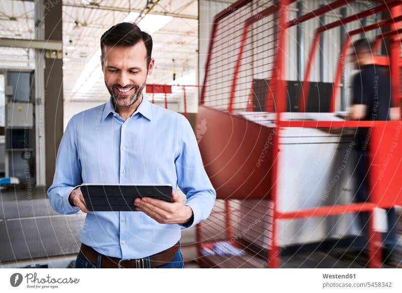 Lächelnder Geschäftsmann mit Tablet in einer Fabrik Job Berufe Berufstätigkeit Beschäftigung Jobs geschäftlich Geschäftsleben Geschäftswelt Geschäftsperson