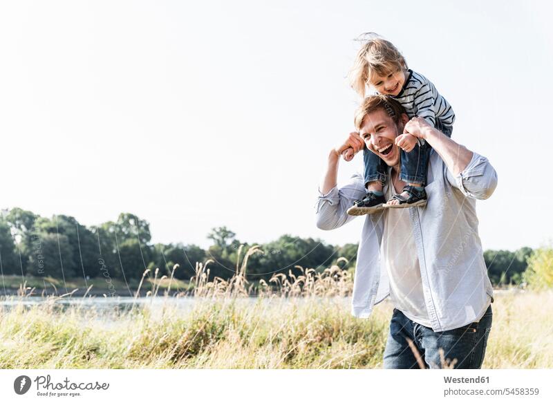 Vater und Sohn haben Spaß am Fluss an einem schönen Sommertag gehen gehend geht auf den Schultern auf der Schulter Kindheit Spaziergang Flussufer Gemeinsamkeit