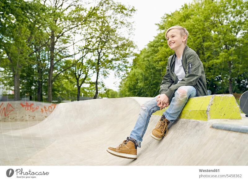 Lachender Junge schaut im Skatepark zur Seite Skateboardpark Skateboard-Park Skateboard Park Skaterplatz sitzen sitzend sitzt Freizeit Muße Seitenblick
