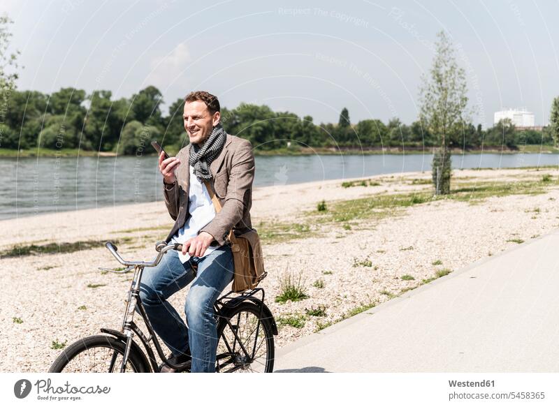 Erwachsener Mann mit Fahrrad mit Smartphone am Rheinufer Bikes Fahrräder Räder Rad iPhone Smartphones Radfahrer Fahrradfahrer Männer männlich telefonieren
