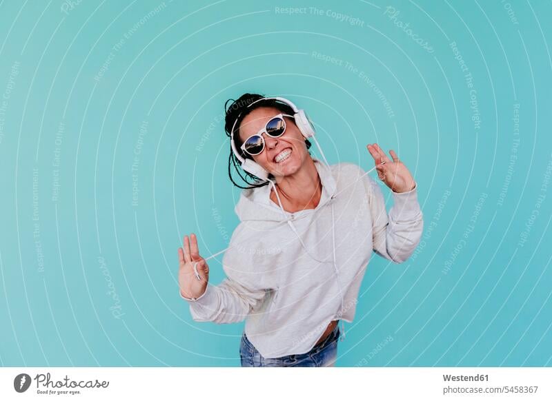 Fröhliche Frau hört Musik, während sie vor türkisfarbenem Hintergrund die Fäden zieht Farbaufnahme Farbe Farbfoto Farbphoto Spanien Freizeitbeschäftigung Muße