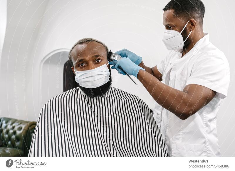 Friseur trägt chirurgische Maske und wiederverwendbare Handschuhe beim Rasieren der Haare des Kunden Leute Menschen People Person Personen Kundschaft Job Berufe