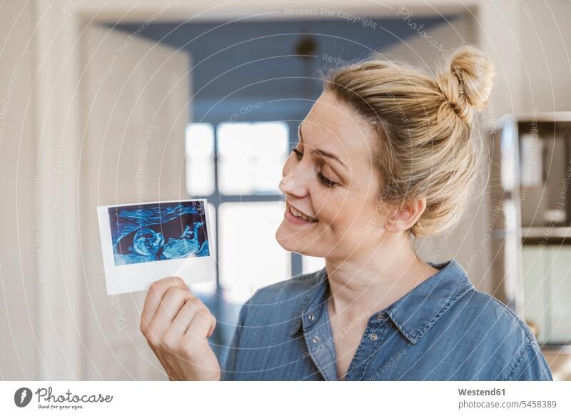 Schwangere Frau hält Ultraschallbild zu Hause Bilder Bildnis freuen Glück glücklich sein glücklichsein zufrieden daheim schwangere Frau Muße drinnen